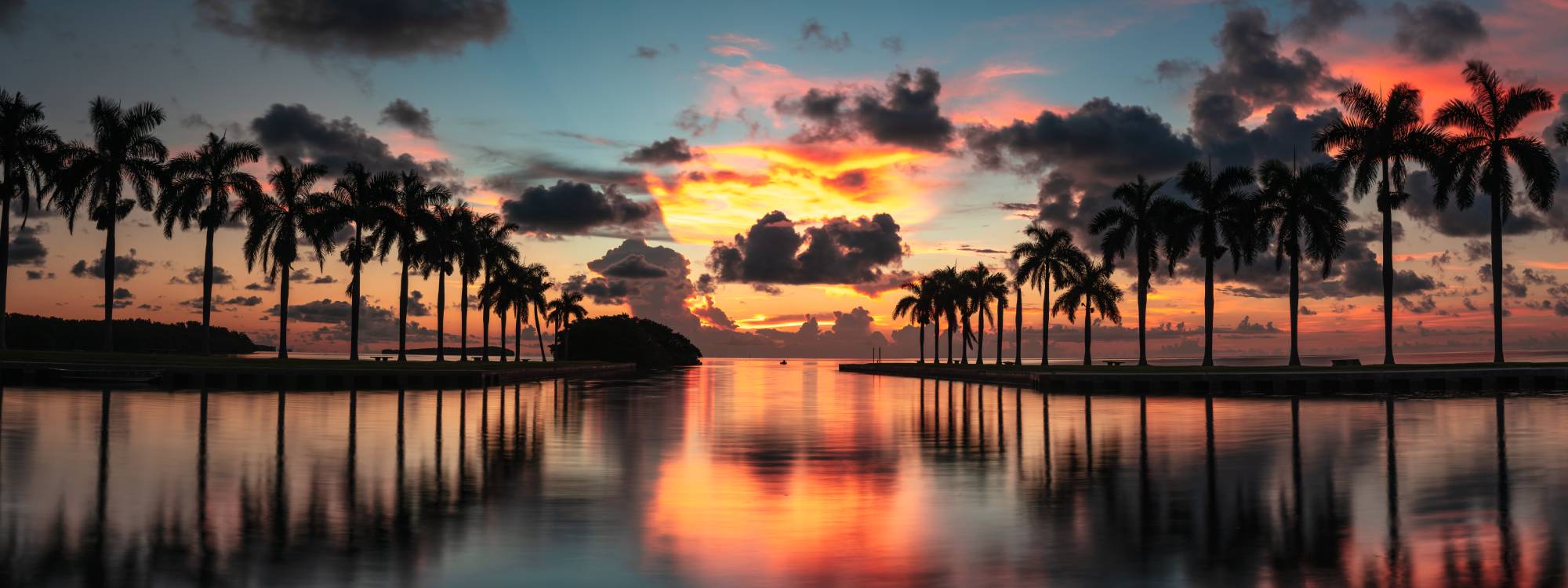 Sunset over palm-lined waterway with reflections